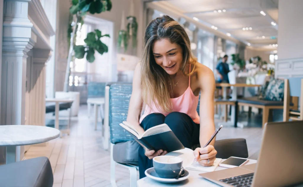 Woman reading a book and writing notes in a bright cafe.